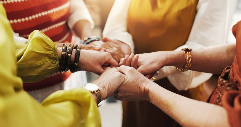 A group of women holds hands in a circle.