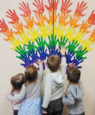 small kids adding colored hand print cut-outs to a wall