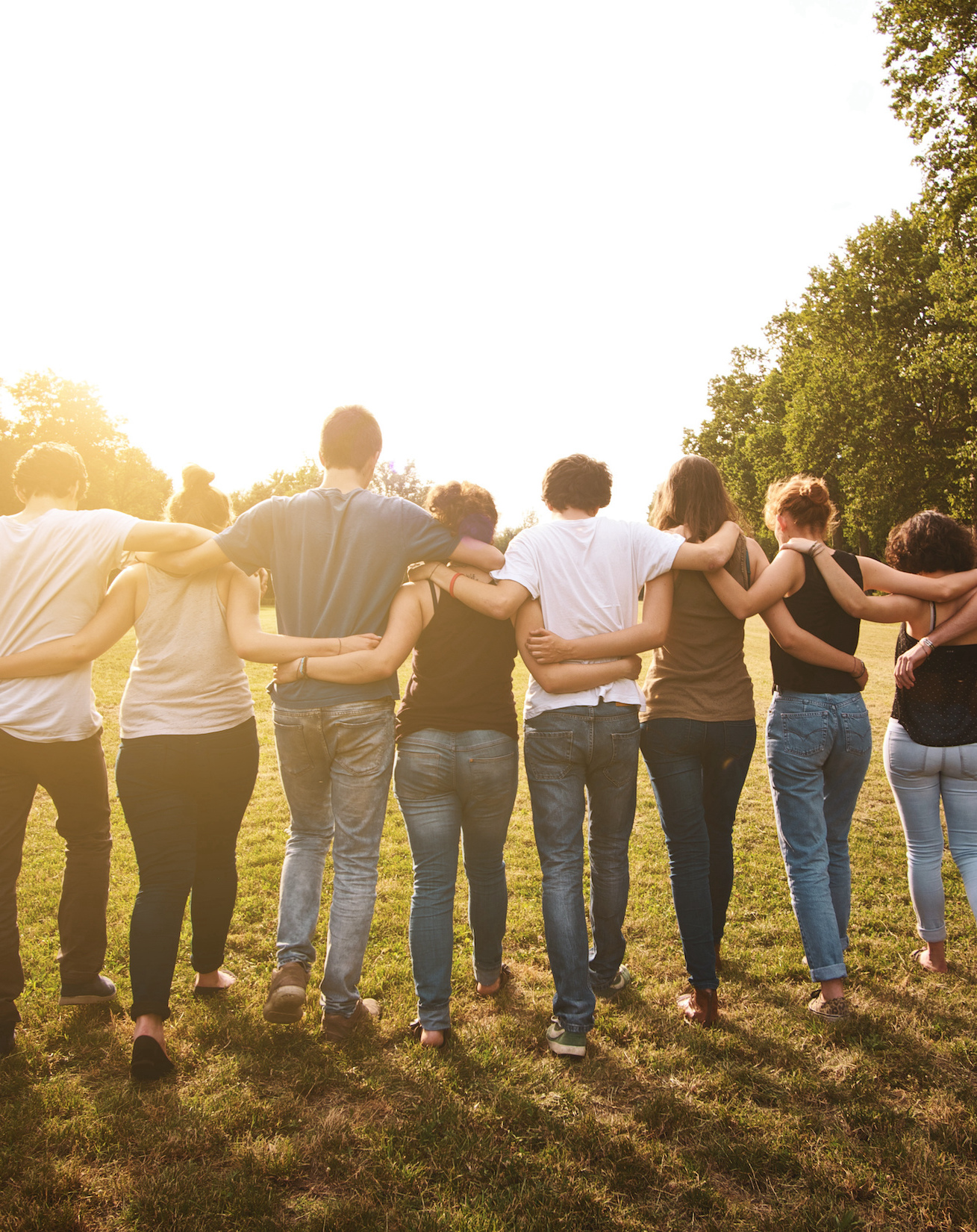 group of people walking on the grass with their arms around each other
