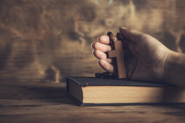 A hand holding a cross on top of a bible.