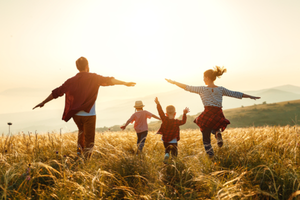A family of four runs through a grassy field at sunset.