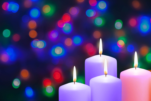 Advent candles burn in front of twinkling Christmas lights.