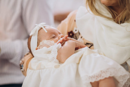 An infant girl in white dress held by her mother and awaiting baptism.