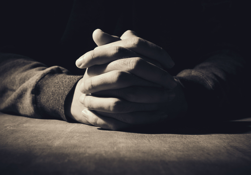 Hands coming out of the darkness and folded in prayer.