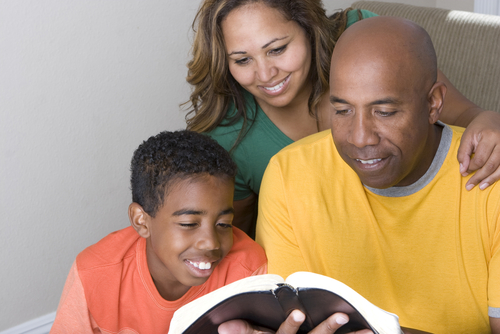 A smiling family reads The Bible together.
