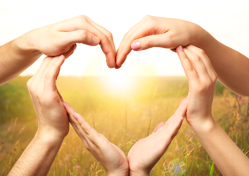 Three sets of hands form a heart in front of a setting sun