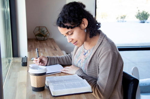 A woman sits at her desk and takes notes as she reads the Bible.
