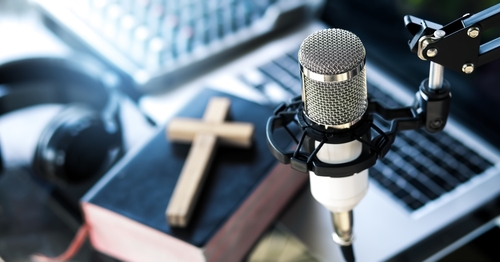 A podcasting microphone with bible and crucifix in the background.