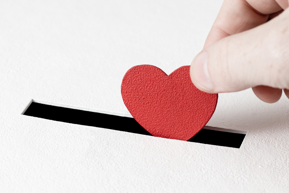 A person depositing a red heart in a coin slot.