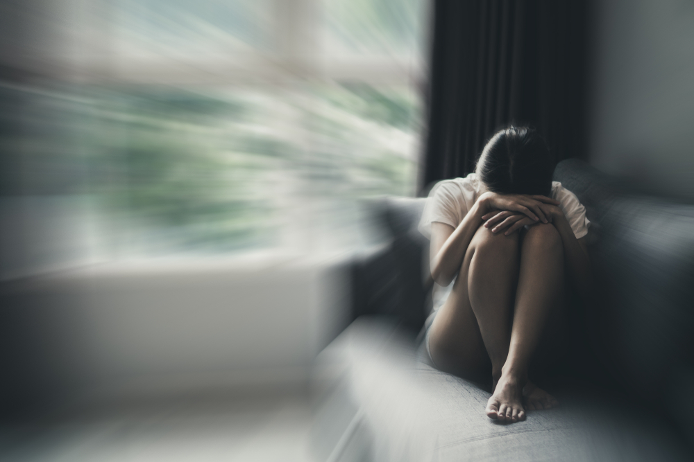 A woman sits with her head down on her couch.