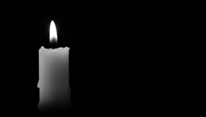 A white candle burns in the dark.