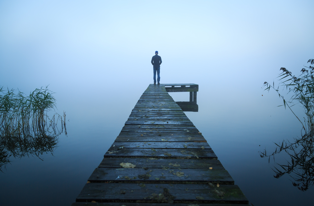 A lone figure stands at the end of a dock on a gray morning.
