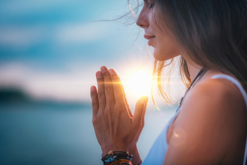 A woman closes her eyes and prays with the sun setting behind her.