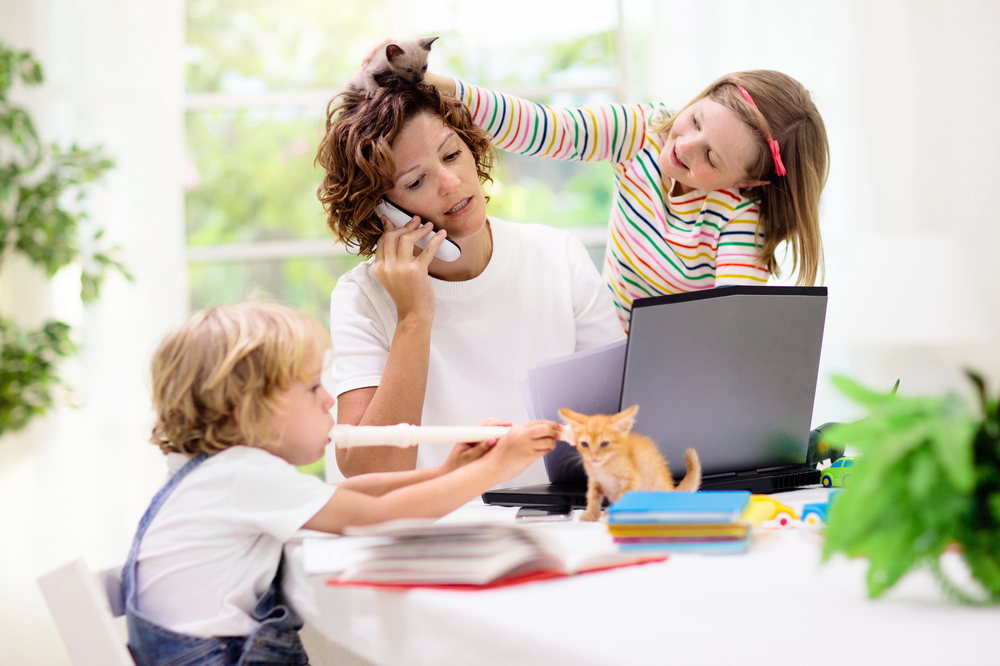 A mom tries to talk on the phone while here kids play with kittens next to her.