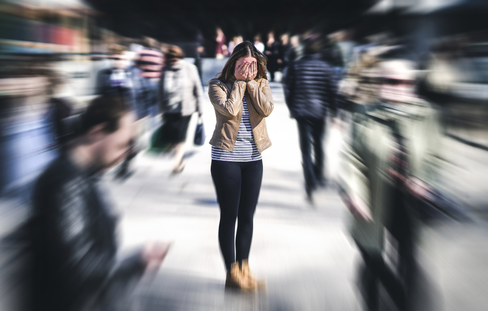 A woman covers her face in a blurred crowd of people.