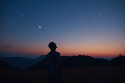 A person in silhouette looks up at the sky around sunset.