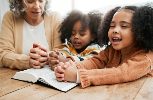 Two little girls pray over a Bible with an older woman.
