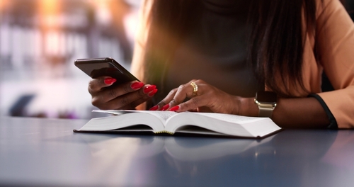 A woman looks at her phone while reading the Bible.