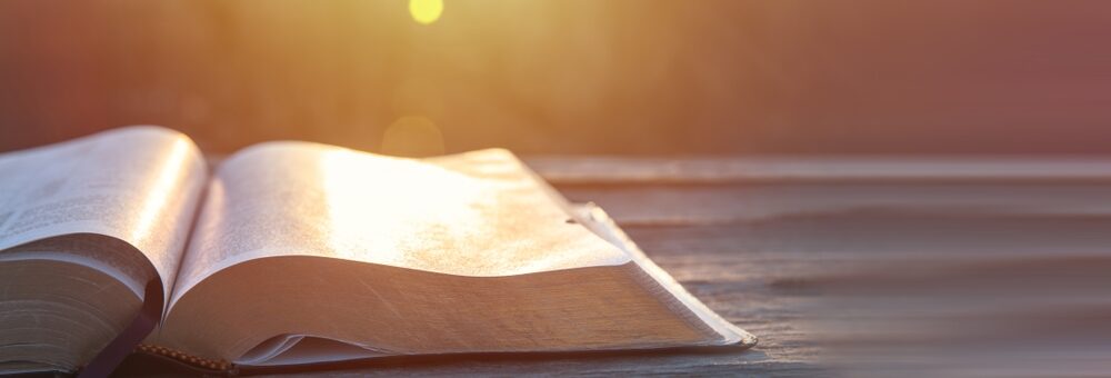 A Bible sits open on a table in the sunshine