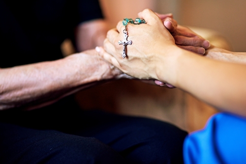 Two people hold hands with a rosary in their hands.