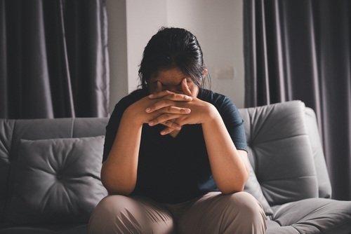 A woman sits on a couch with her head in her hands. 