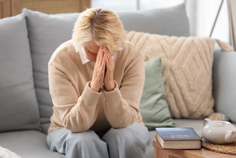 An older woman prays next to a Bible.