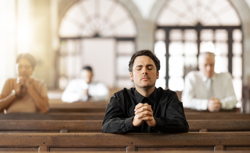 A man prays inside a sunny church.