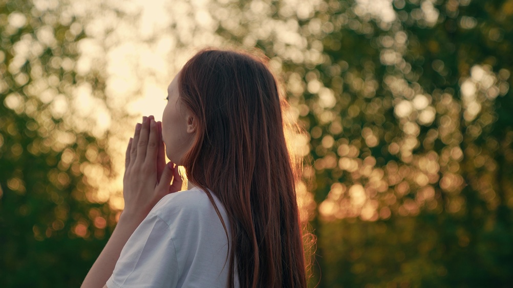A woman prays while outdoors.